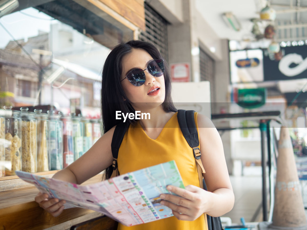 Young woman holding map standing by concession stand in city