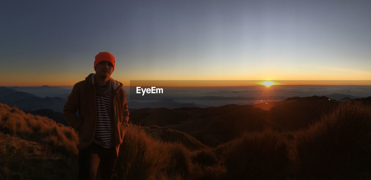 Man standing on shore against sky during sunset