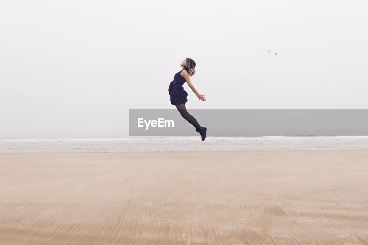 Full length of woman jumping at beach against sky