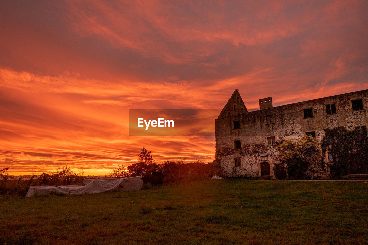 BUILDINGS ON FIELD AGAINST ORANGE SKY