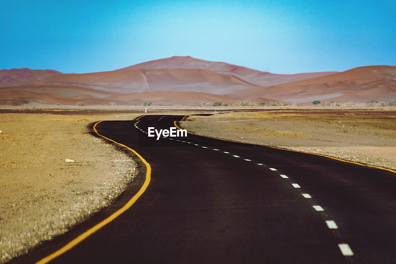 Empty road leading towards mountain against sky