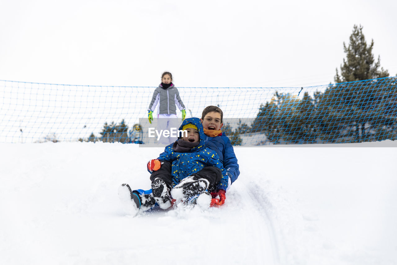 Full length of siblings tobogganing on snow during winter