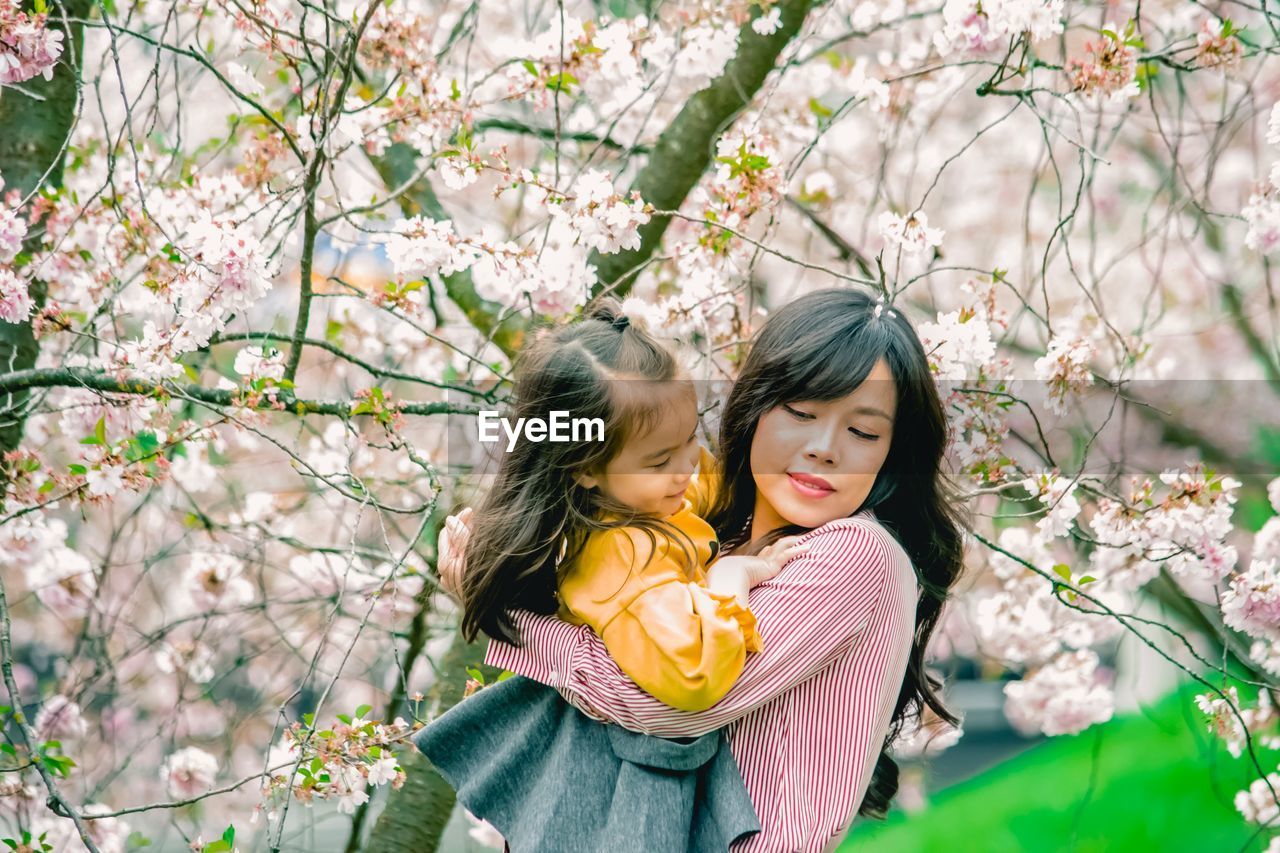 Beautiful young woman carrying daughter by cherry tree