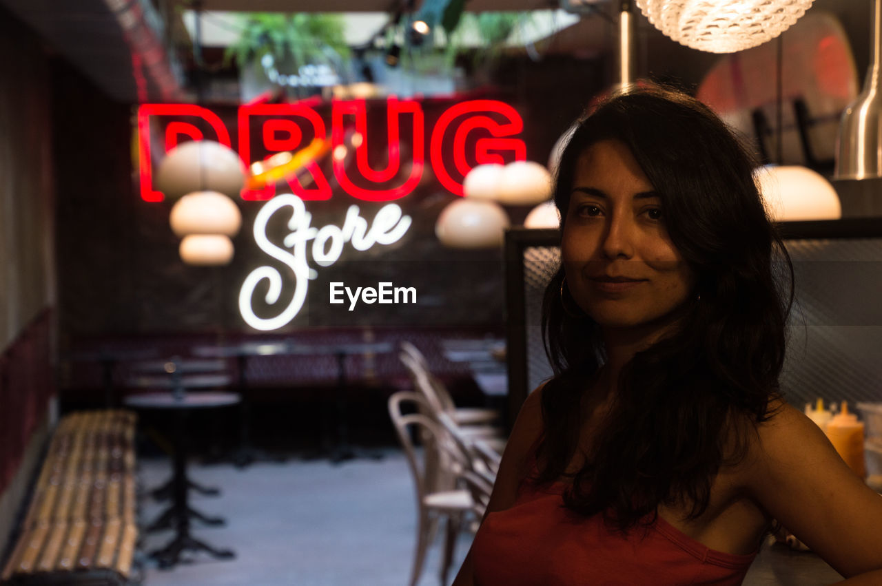 PORTRAIT OF YOUNG WOMAN WITH TEXT ON ILLUMINATED SIGN