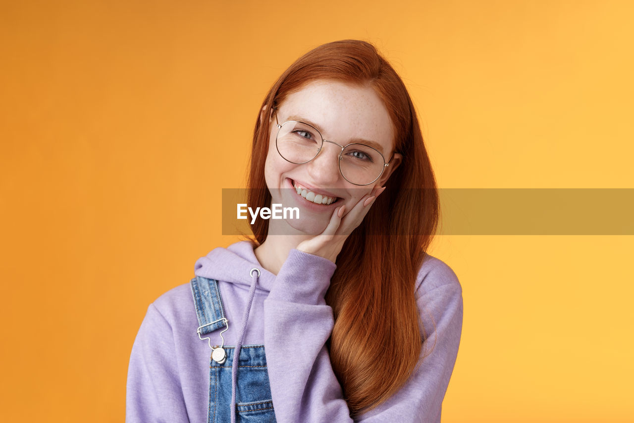 Woman in eyeglasses with hand on cheek against yellow background