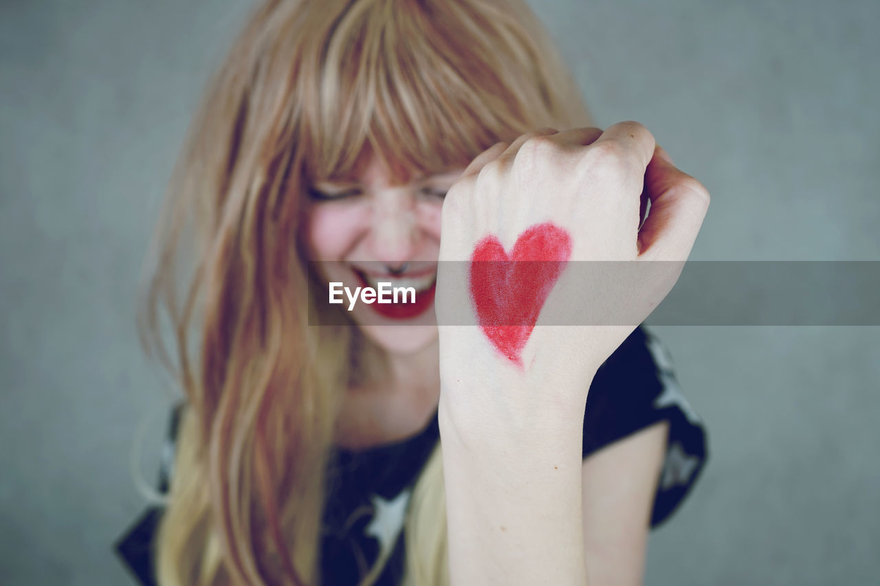 Happy young woman with heart shape on hand against gray background