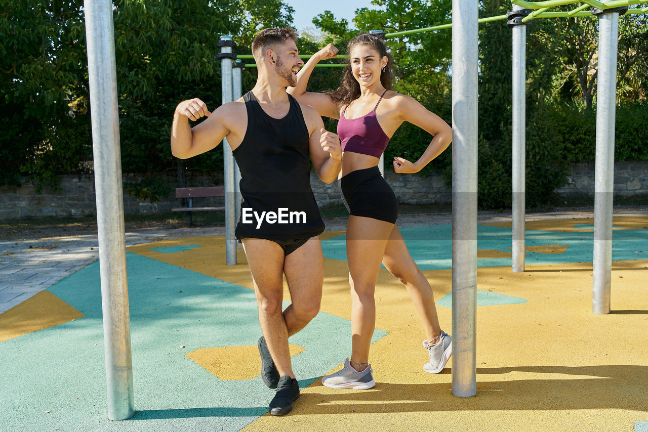 Young man and woman posing in a calisthenics park on a sunny day