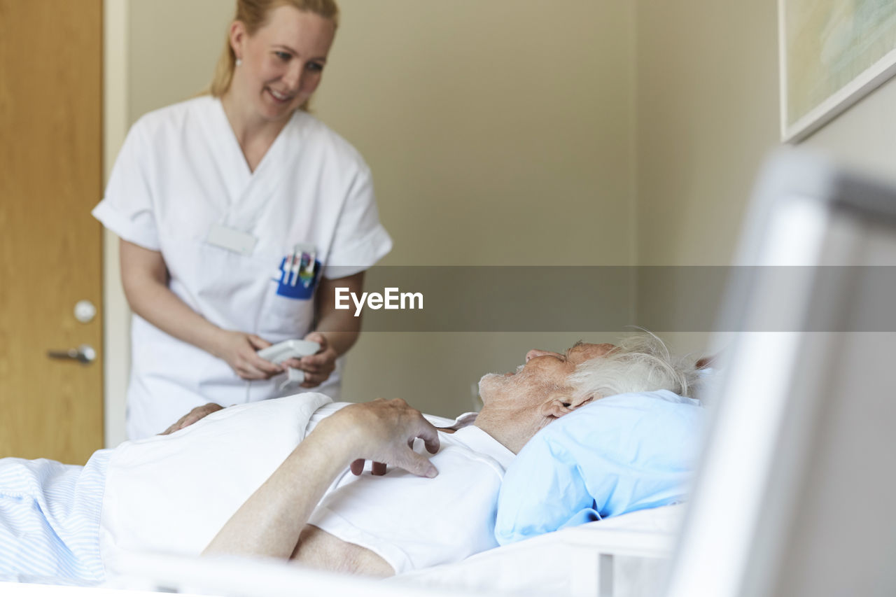 Smiling female nurse adjusting bed senior man's bed in hospital ward