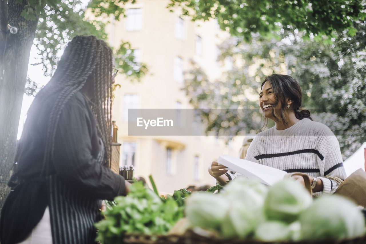 Low angle view of happy customer discussing with vegetable market while doing shopping at market