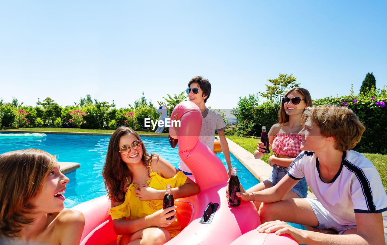 portrait of smiling friends in swimming pool against sky