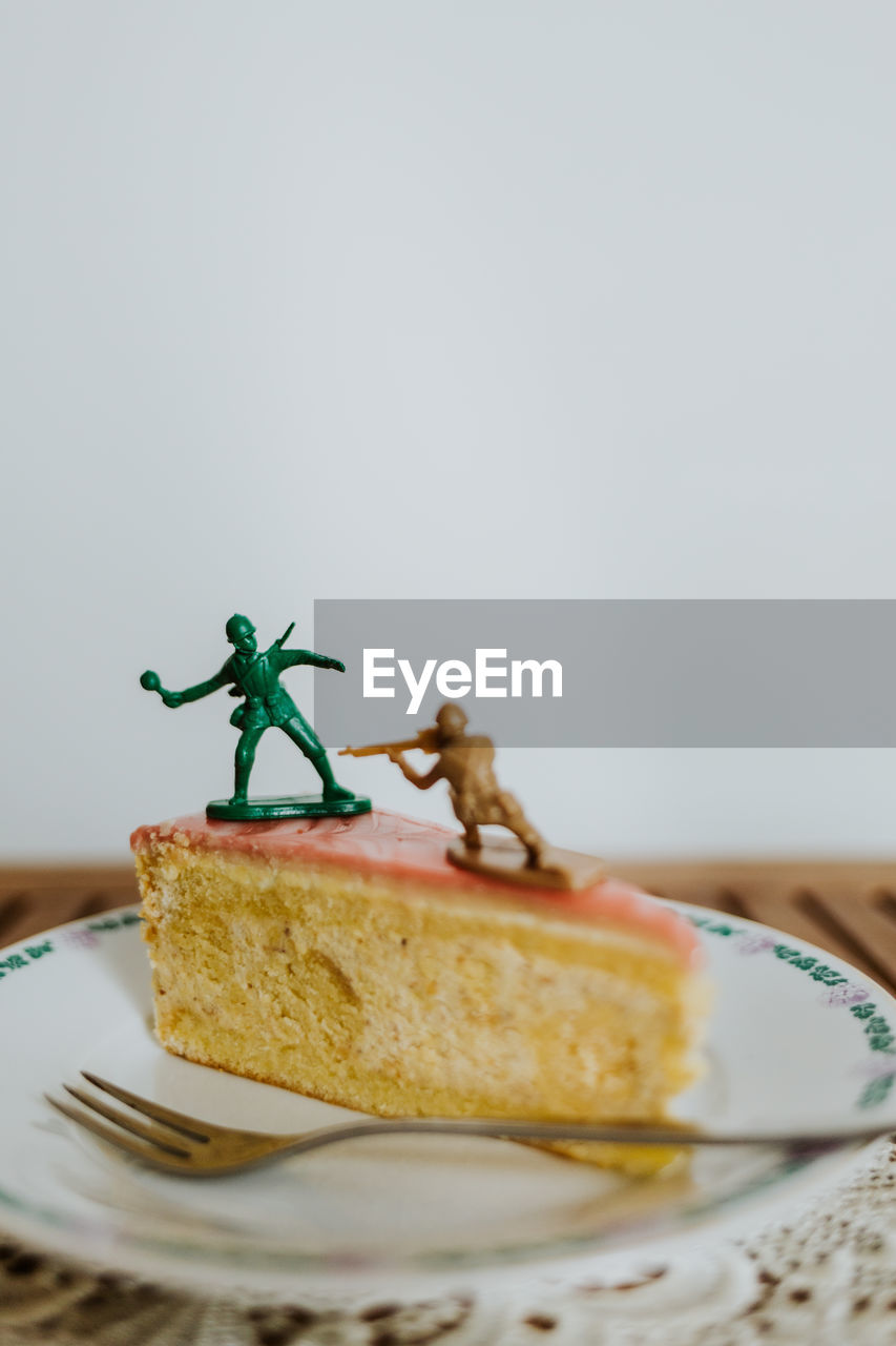 Close-up of dessert in plate with toy soldiers fighting on it against white background 