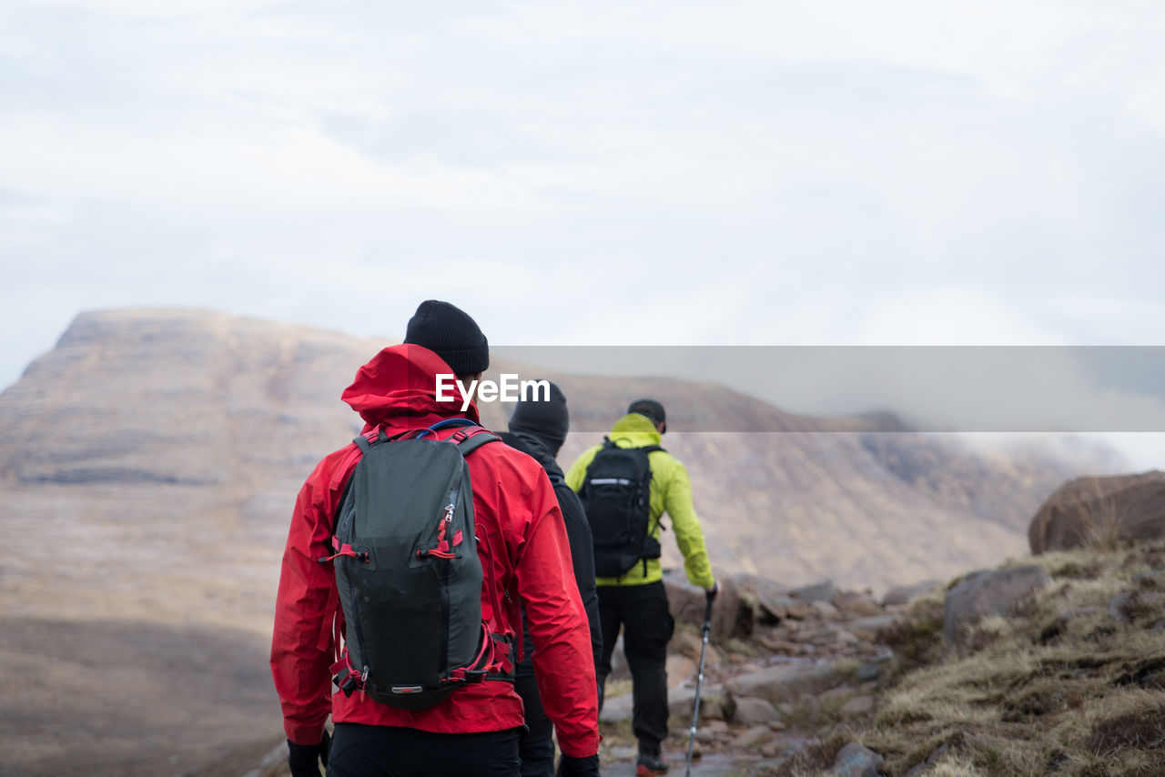 Rear view of male hikers hiking on mountain against cloudy sky