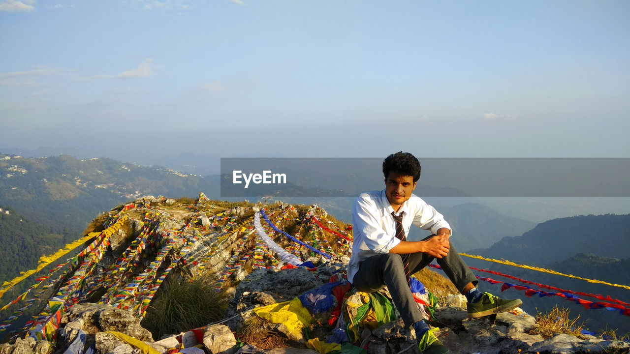 Young man sitting on mountain with prayer flags against sky