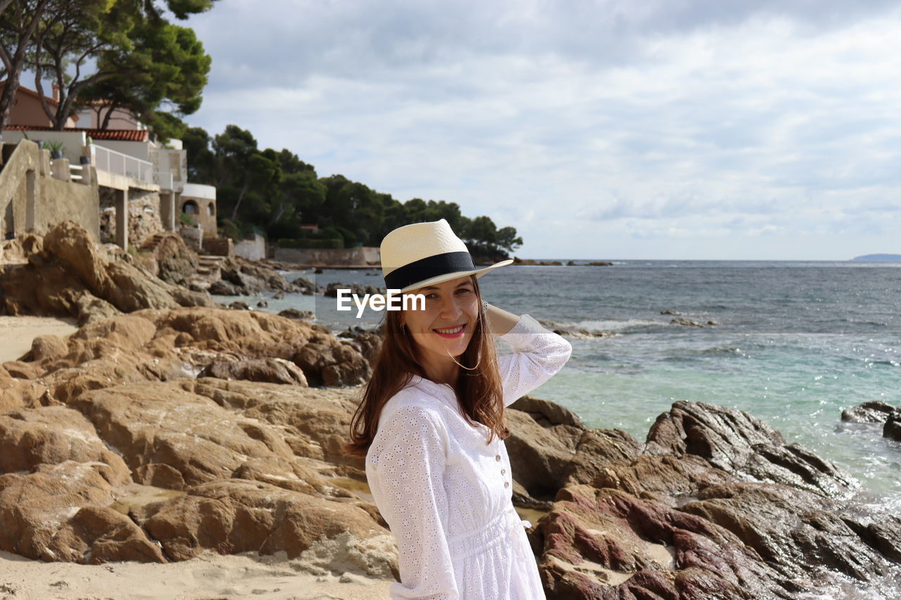 Portrait of woman sitting on rock by sea against sky