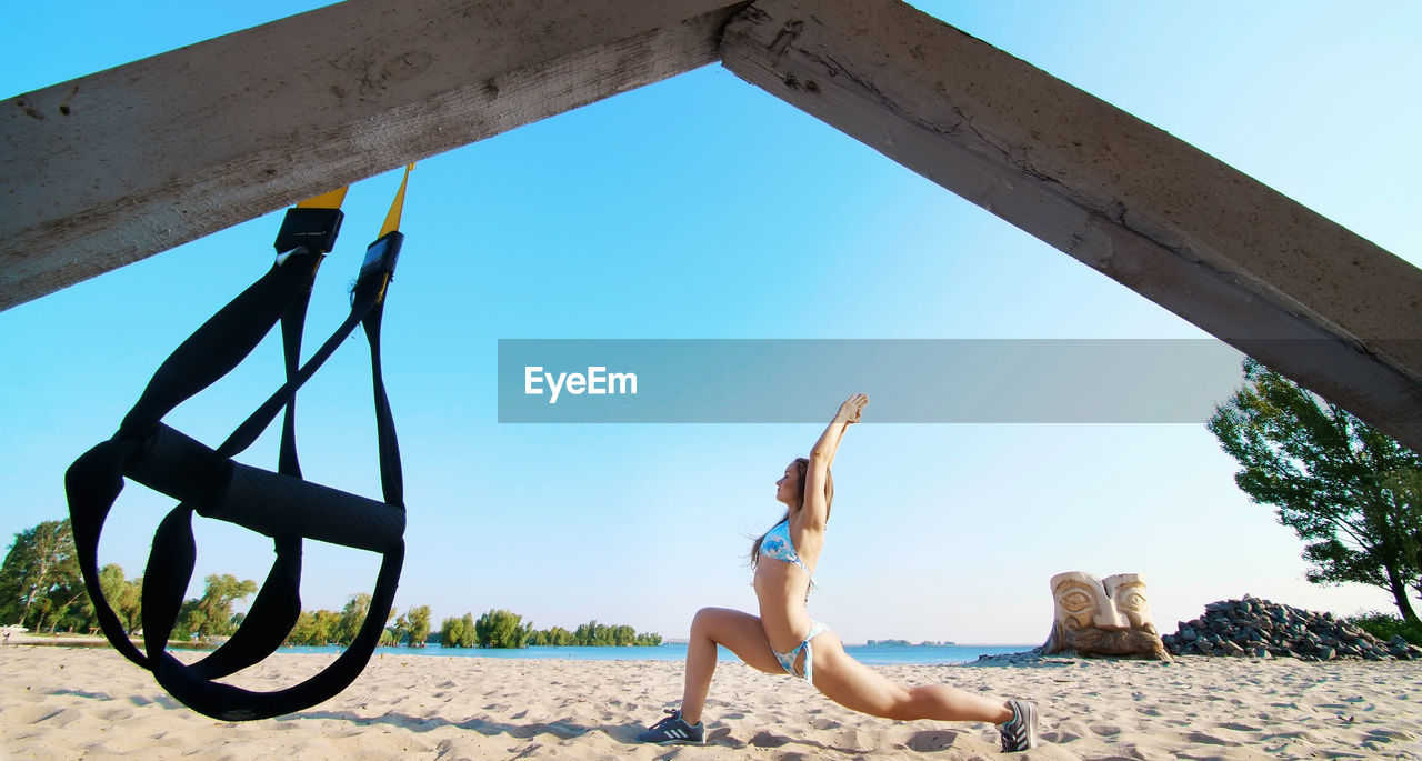 Athletic, young woman in swimsuit doing stretching, balance exercises. close-up. on the beach