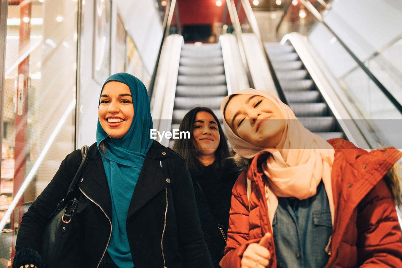 Portrait of happy female friends on escalator in shopping mall