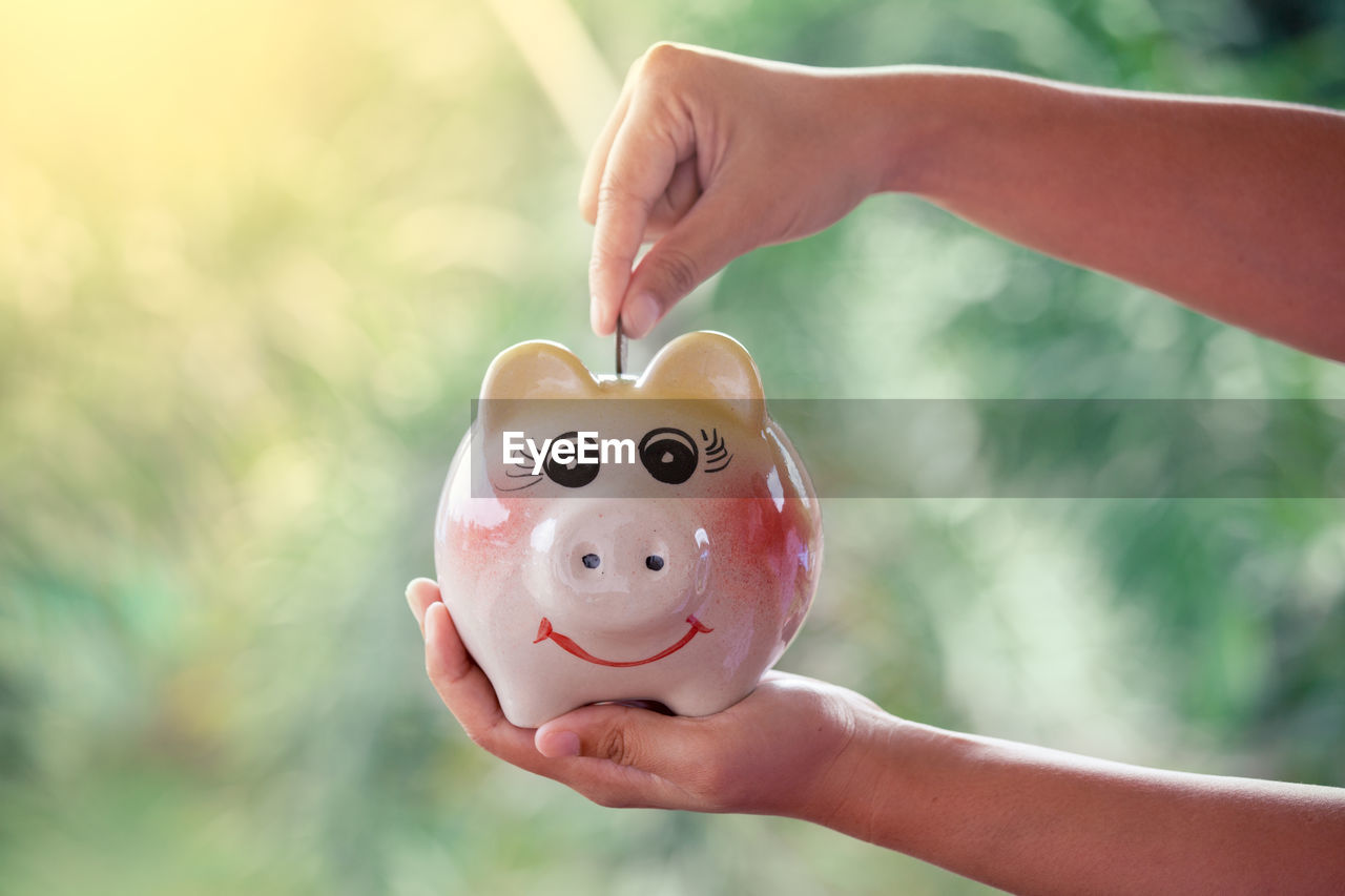 Cropped hand of woman putting coin in piggy bank