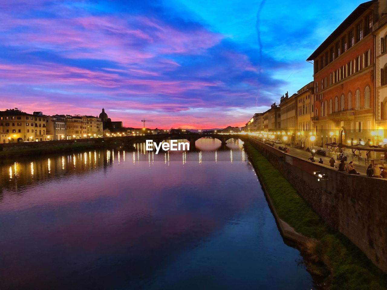 CANAL AMIDST ILLUMINATED CITY BUILDINGS AT SUNSET