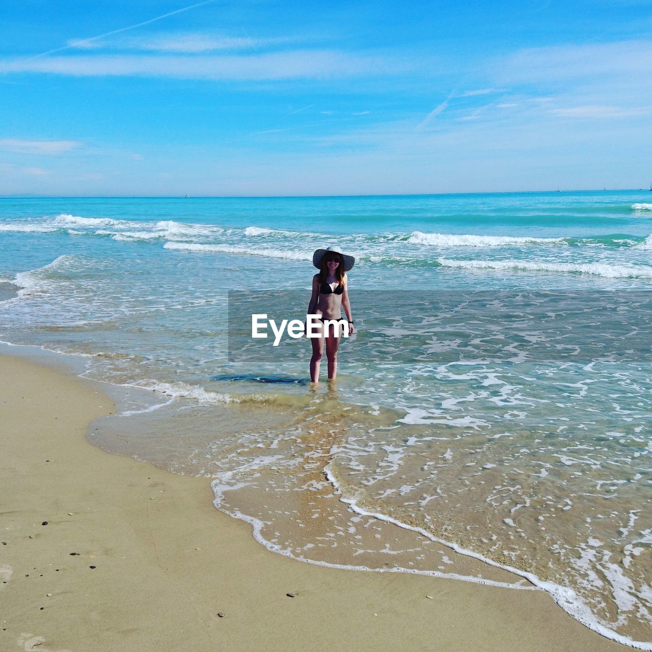 Young woman in bikini standing on shore at beach during sunny day