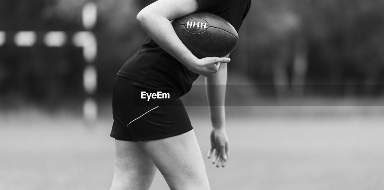 Midsection of woman holding american football while standing outdoors