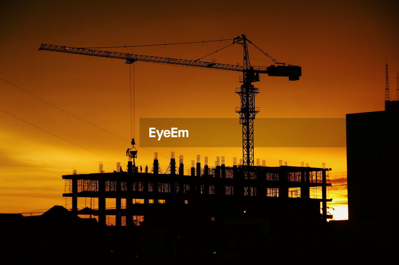 Silhouette crane at construction site during sunset