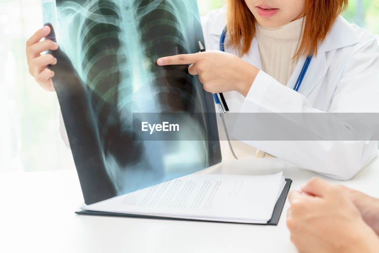 Midsection of female doctor showing chest x-ray to patient in hospital