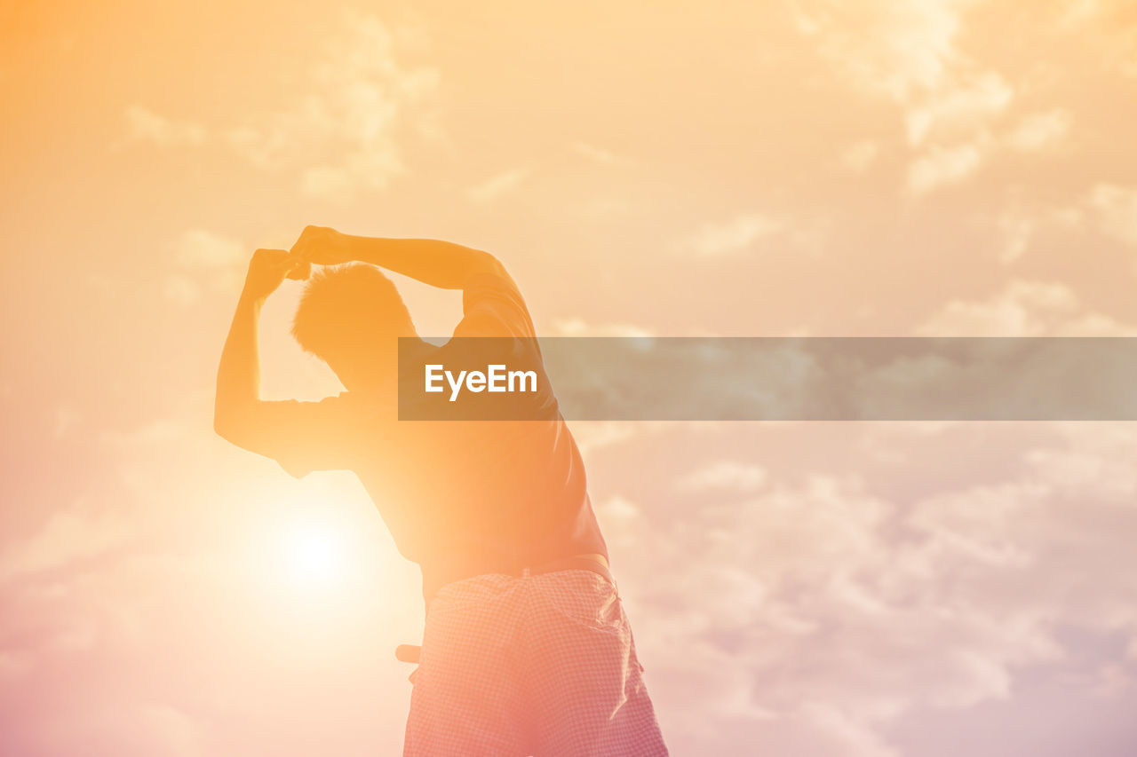 Silhouette man with arms raised standing against sky during sunset