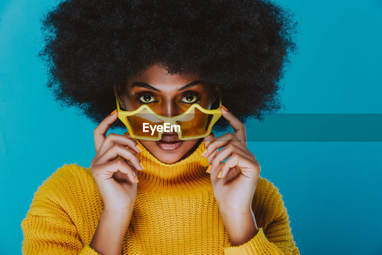 Portrait of smiling young woman holding star shape sunglasses against blue background