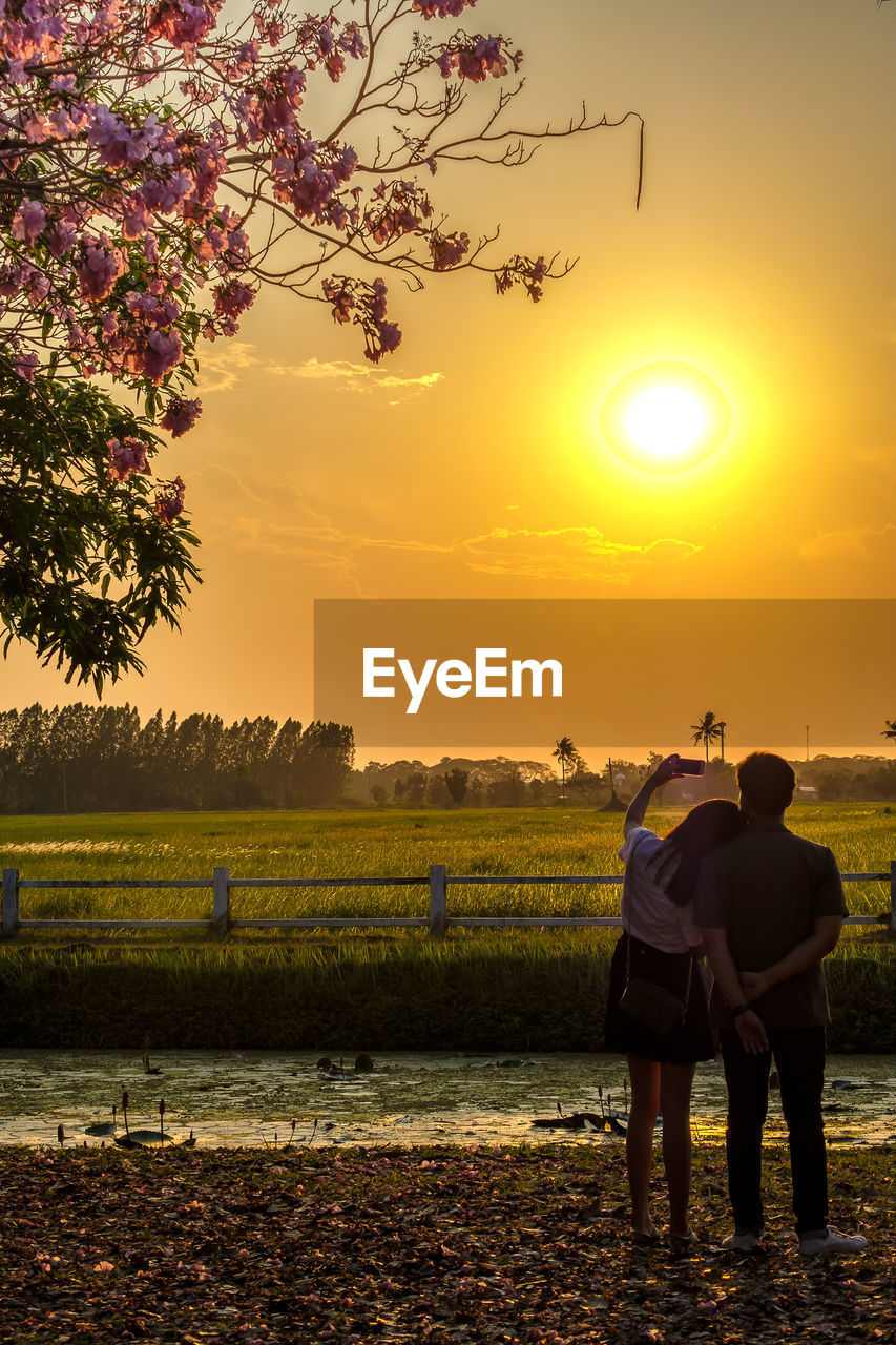 REAR VIEW OF MEN ON FIELD AGAINST SUNSET SKY