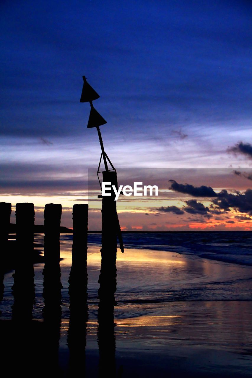 Silhouette wooden posts on beach against sky at sunset