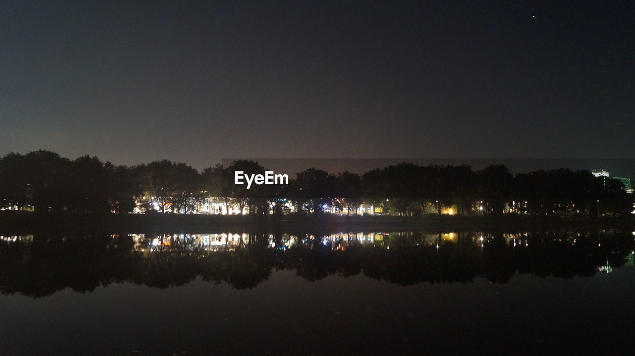 REFLECTION OF ILLUMINATED TREES IN CALM LAKE