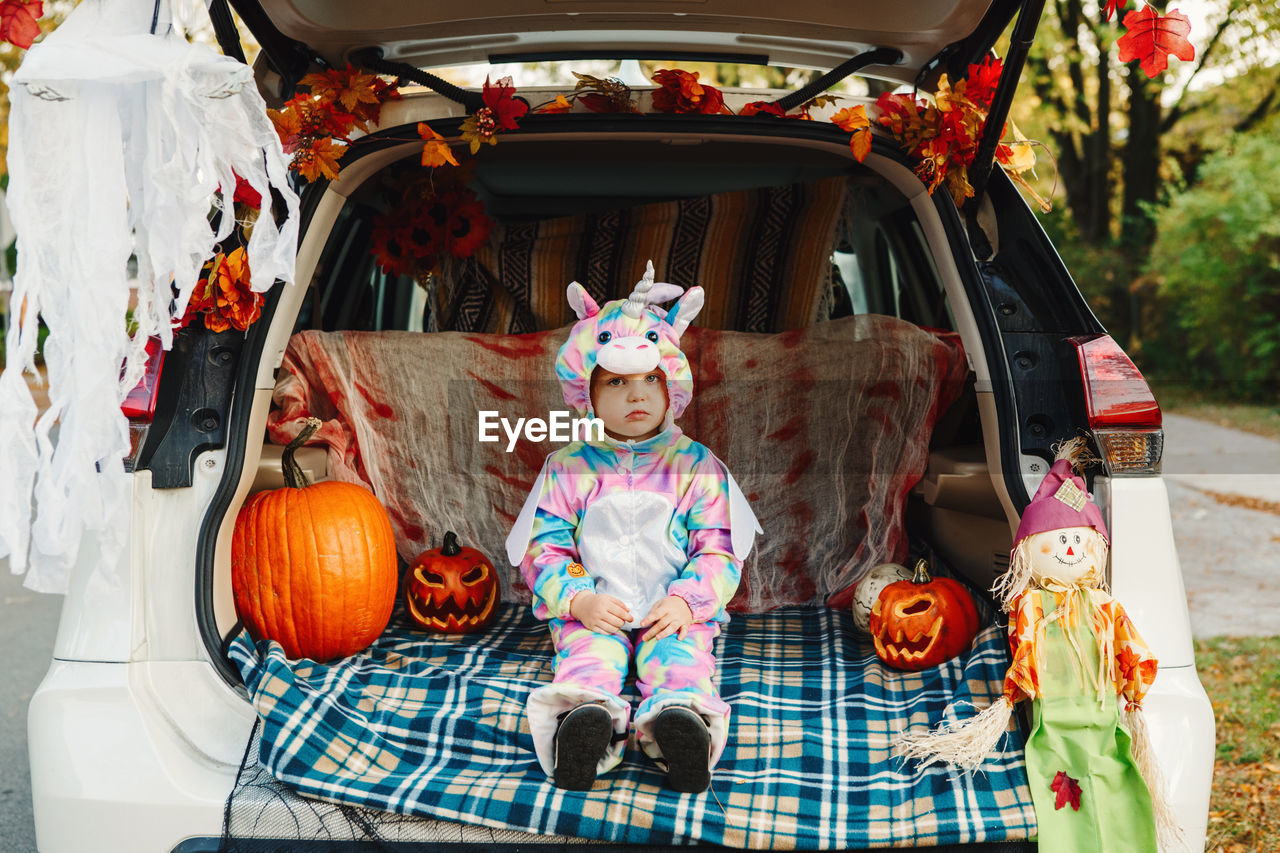 Trick or trunk. sad upset baby in unicorn costume celebrating halloween in trunk of a car. 