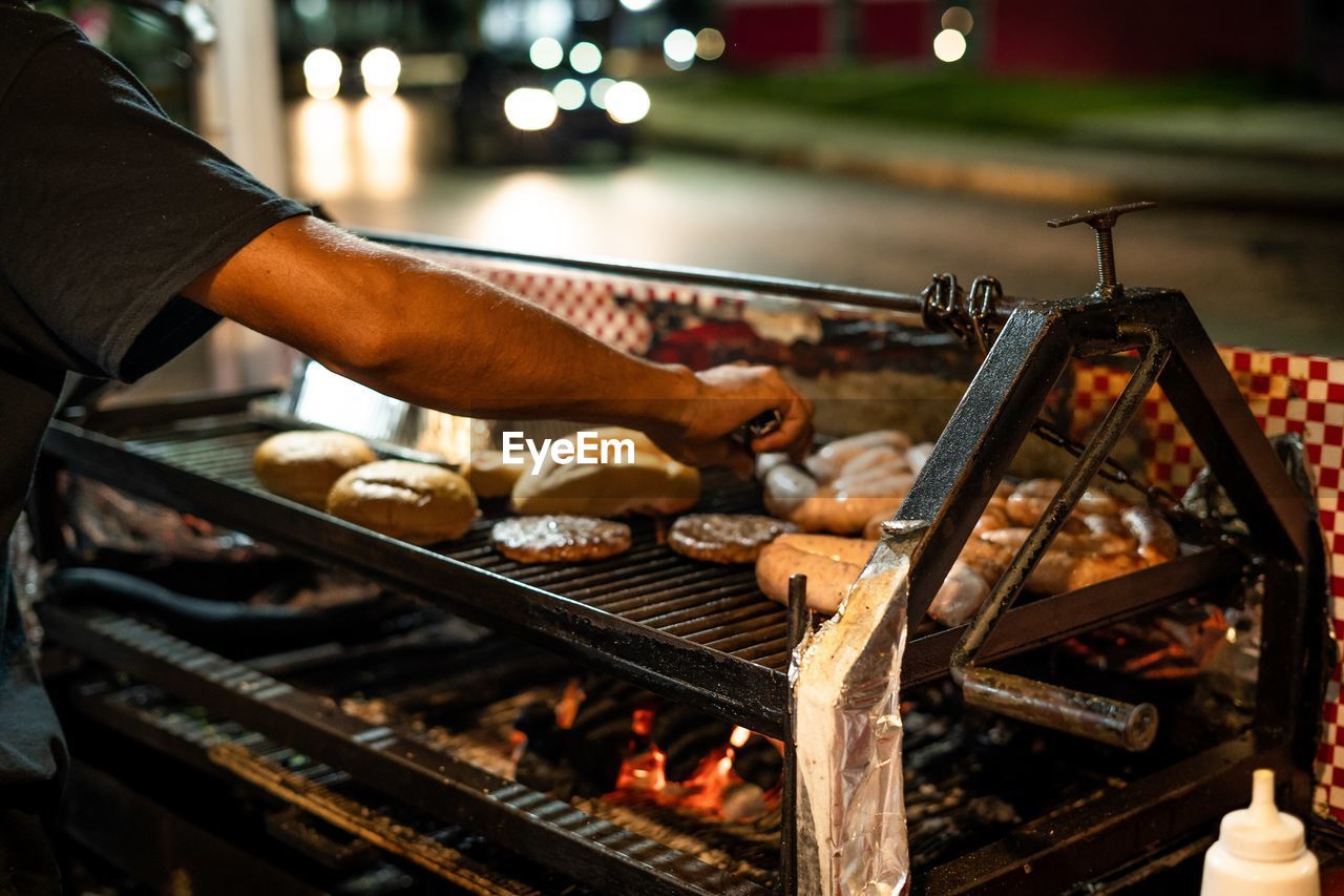 food and drink, food, barbecue, heat, barbecue grill, fast food, freshness, meat, one person, hand, grilled, preparing food, adult, night, men, grilling, burning, occupation, fire, focus on foreground, sausage, outdoors, business