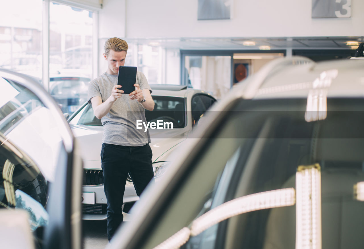 Man photographing car through digital tablet at dealership store