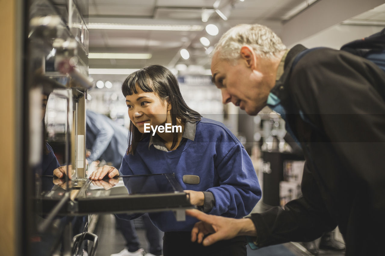 Saleswoman and mature customer looking at oven while standing in electronics store