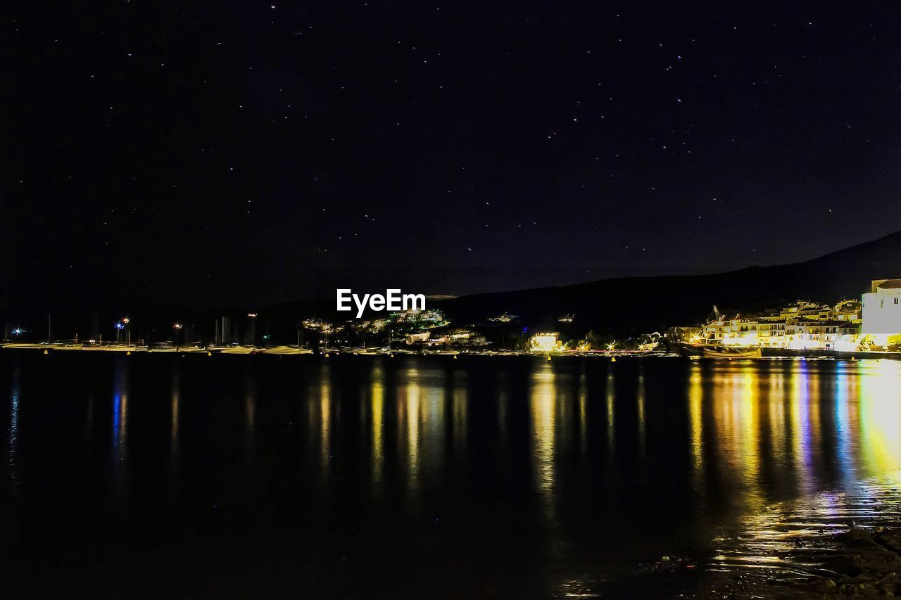 ILLUMINATED BUILDING BY LAKE AGAINST SKY AT NIGHT