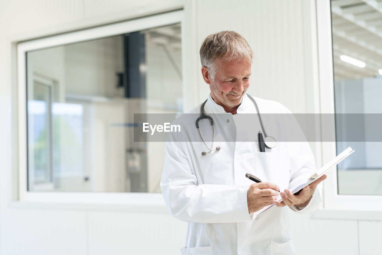 Smiling doctor writing on document at clinic