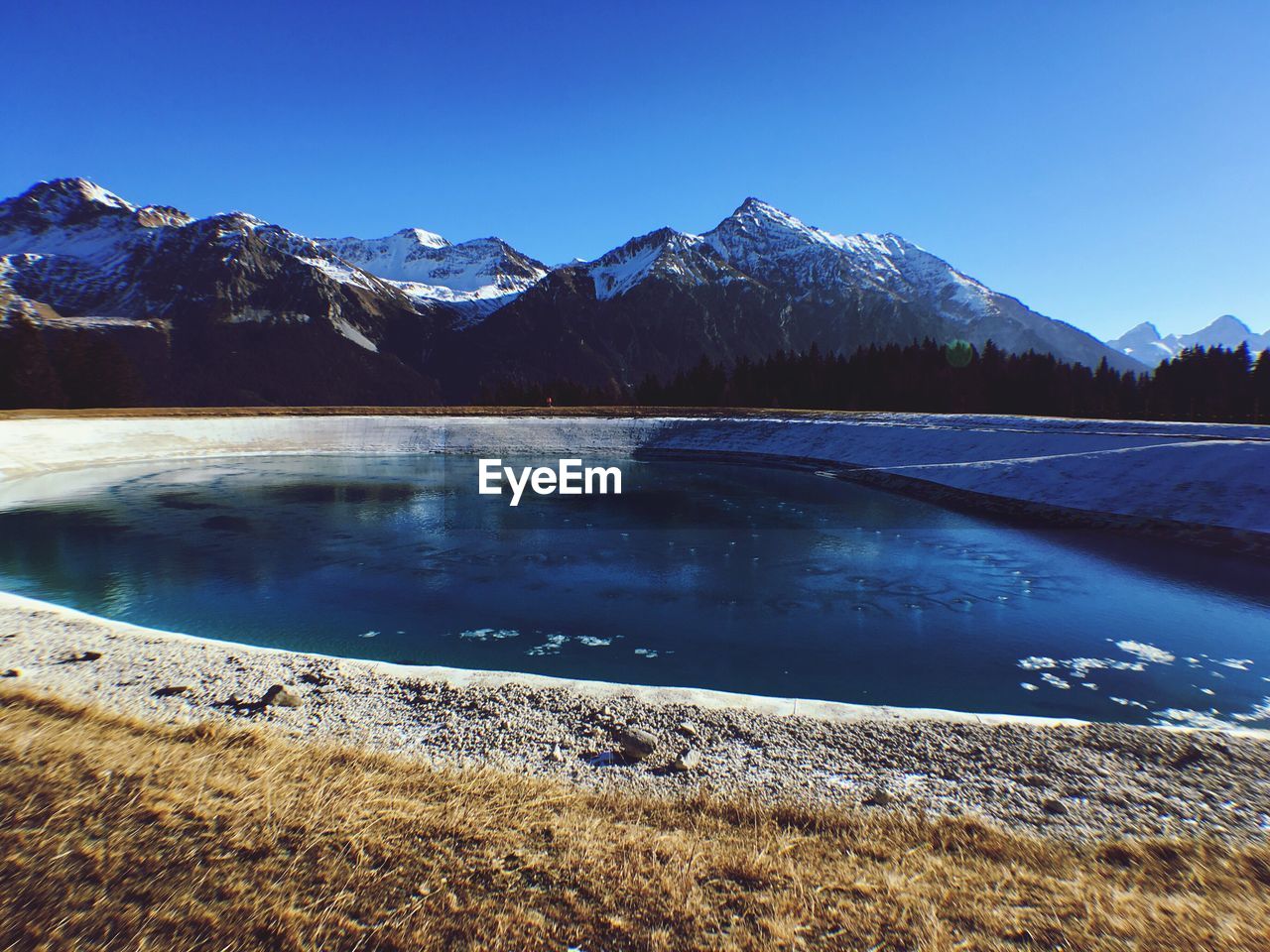 Scenic view of lake and mountains against clear blue sky