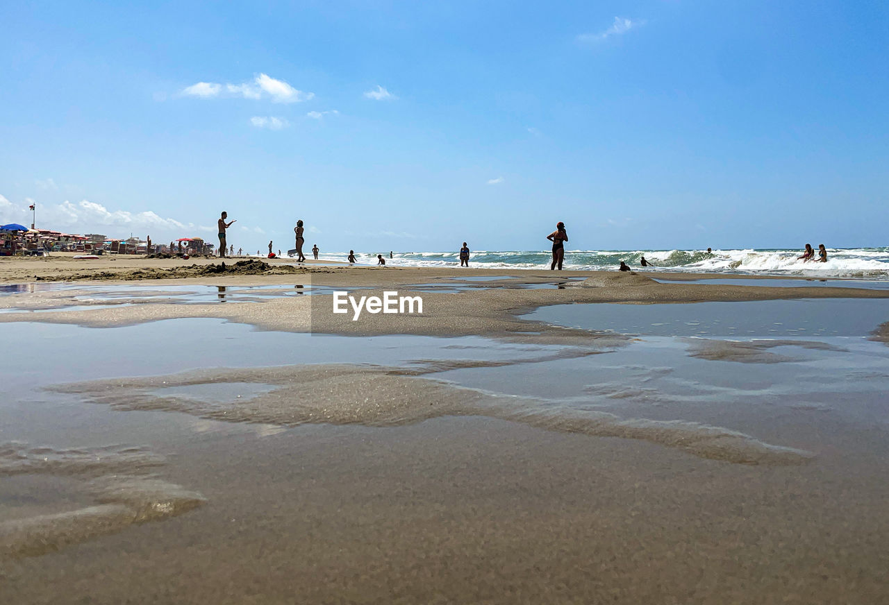 water, land, sea, beach, shore, sky, body of water, sand, coast, ocean, nature, group of people, holiday, travel, wave, scenics - nature, beauty in nature, vacation, trip, bay, day, travel destinations, environment, large group of people, horizon, tourism, blue, cloud, outdoors, sunny, men, landscape, coastline, adult, tide, tranquility, tourist, walkway, low tide, water's edge, leisure activity, wind wave, crowd, summer, sunlight