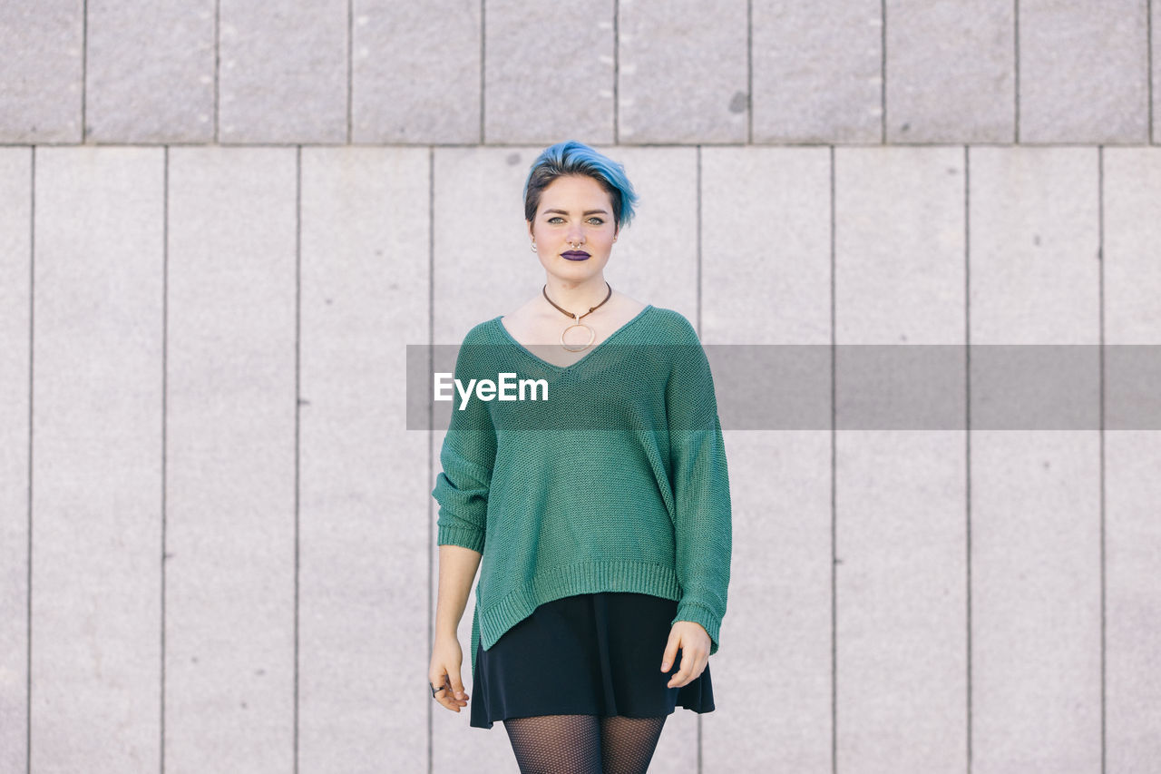 PORTRAIT OF A WOMAN STANDING AGAINST WALL