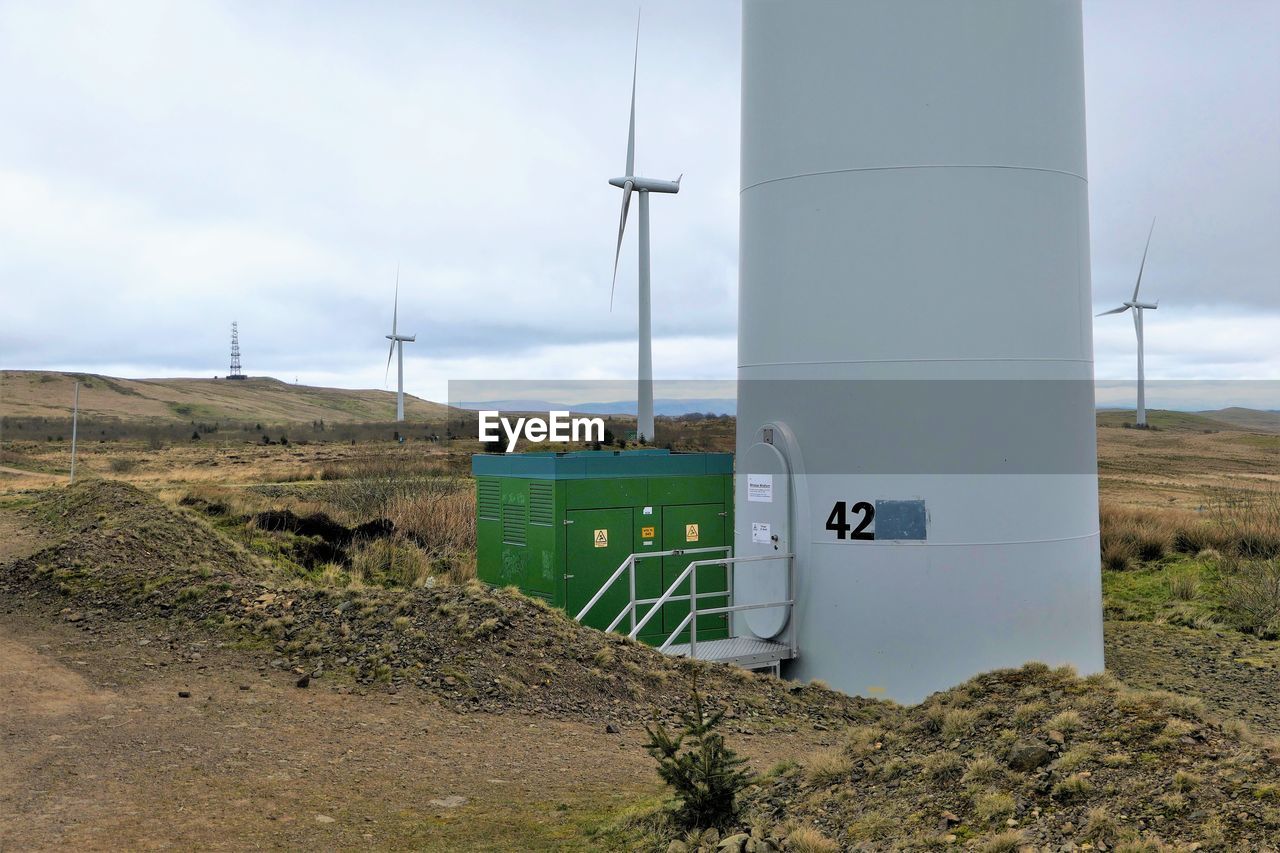 Close-up view of wind turbine base in field against sky