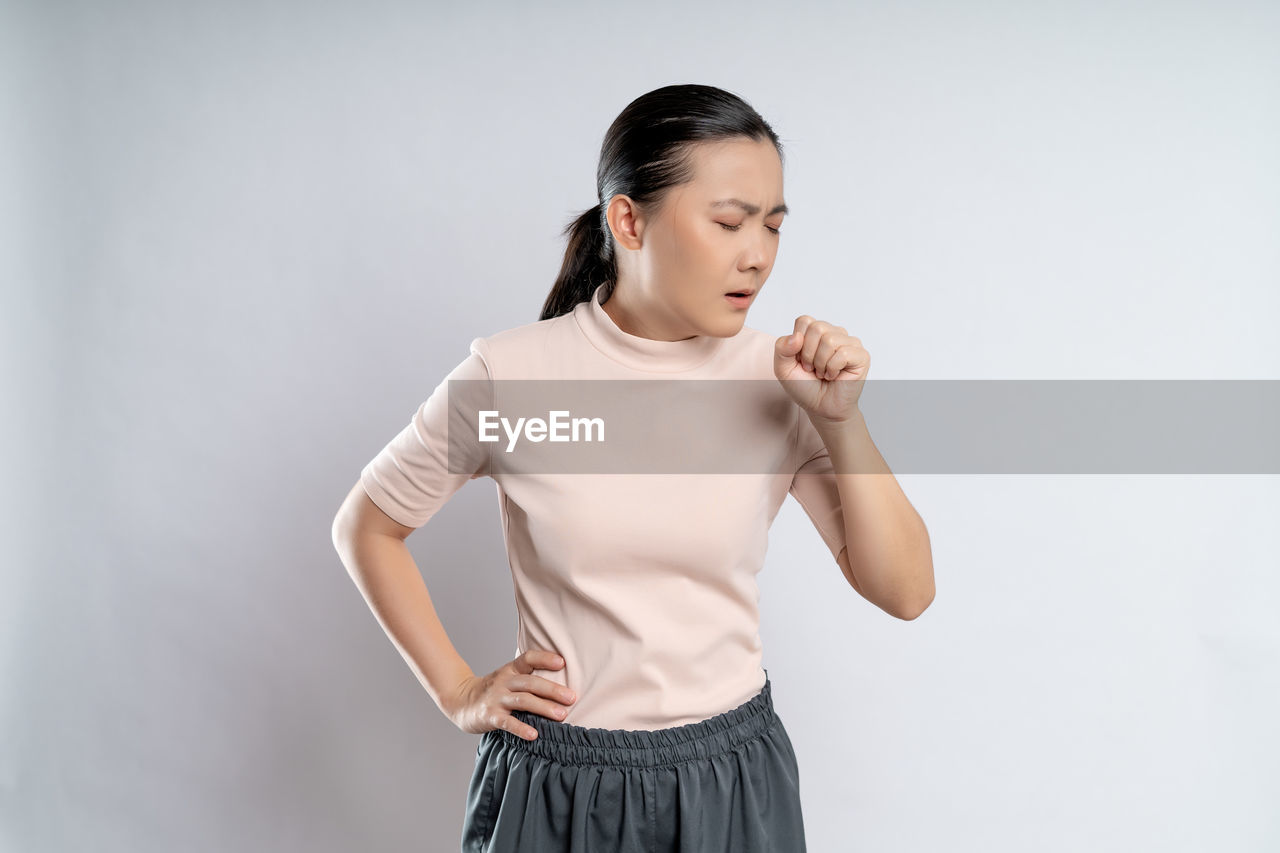 one person, studio shot, indoors, women, sleeve, adult, gray, clothing, gray background, standing, photo shoot, young adult, copy space, portrait, emotion, lifestyles, skirt, exercising, female, t-shirt, front view, hand, trunk, waist up, looking, white background, white, arm, hairstyle, strength, vitality