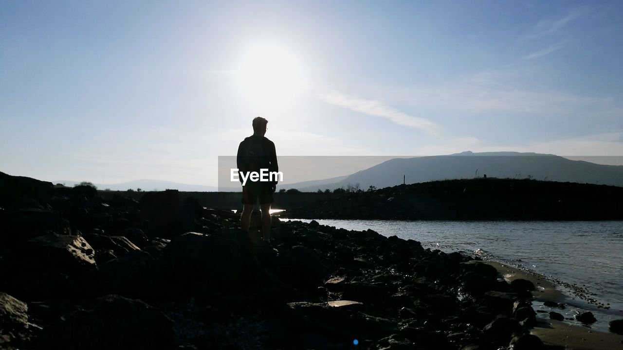 Rear view of man standing on rocks by sea