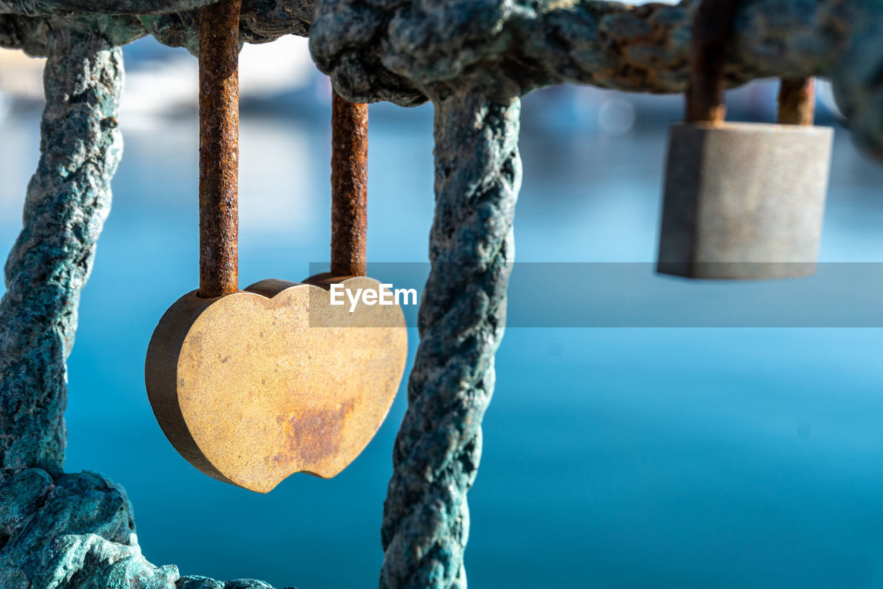Close-up of a rusty heart-shaped padlock, with an out-of-focus sea background.