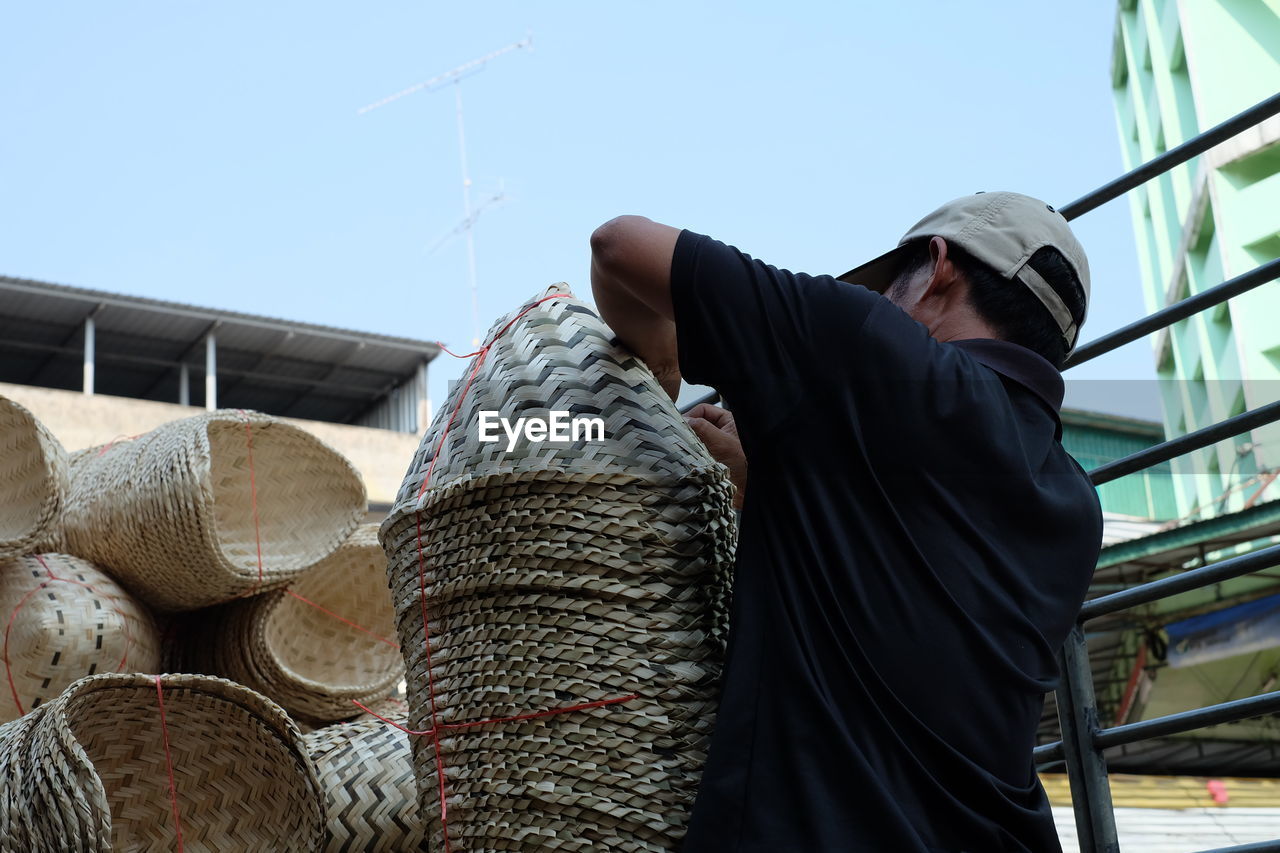 Man stacking basket while standing against sky