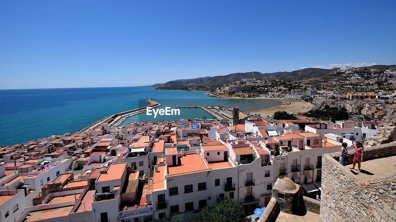 PANORAMIC VIEW OF TOWNSCAPE BY SEA AGAINST CLEAR SKY