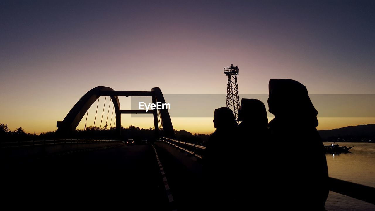 Silhouette people on bridge against sky during sunset