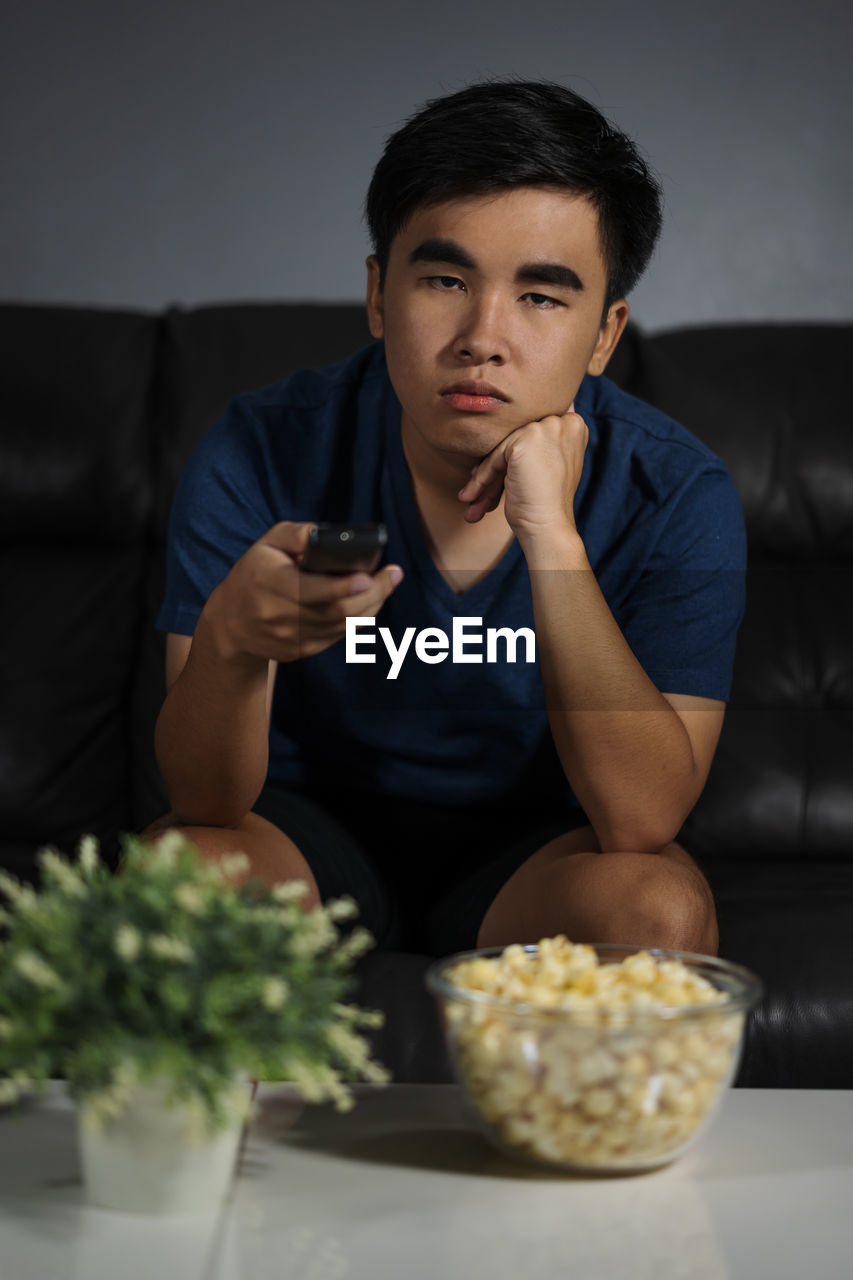 YOUNG MAN LOOKING AWAY WHILE SITTING AT TABLE