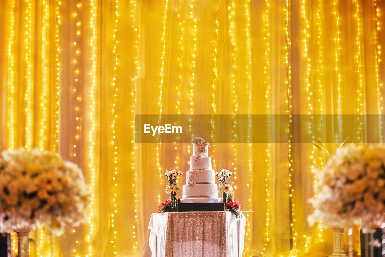 Layered cake on table against illuminated curtain