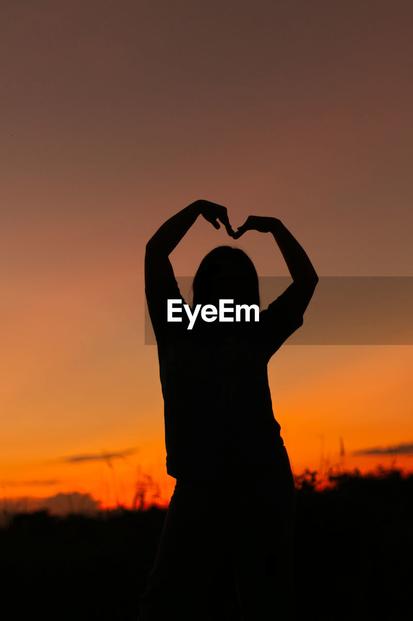 Woman gesturing success - silhouette over evening sky